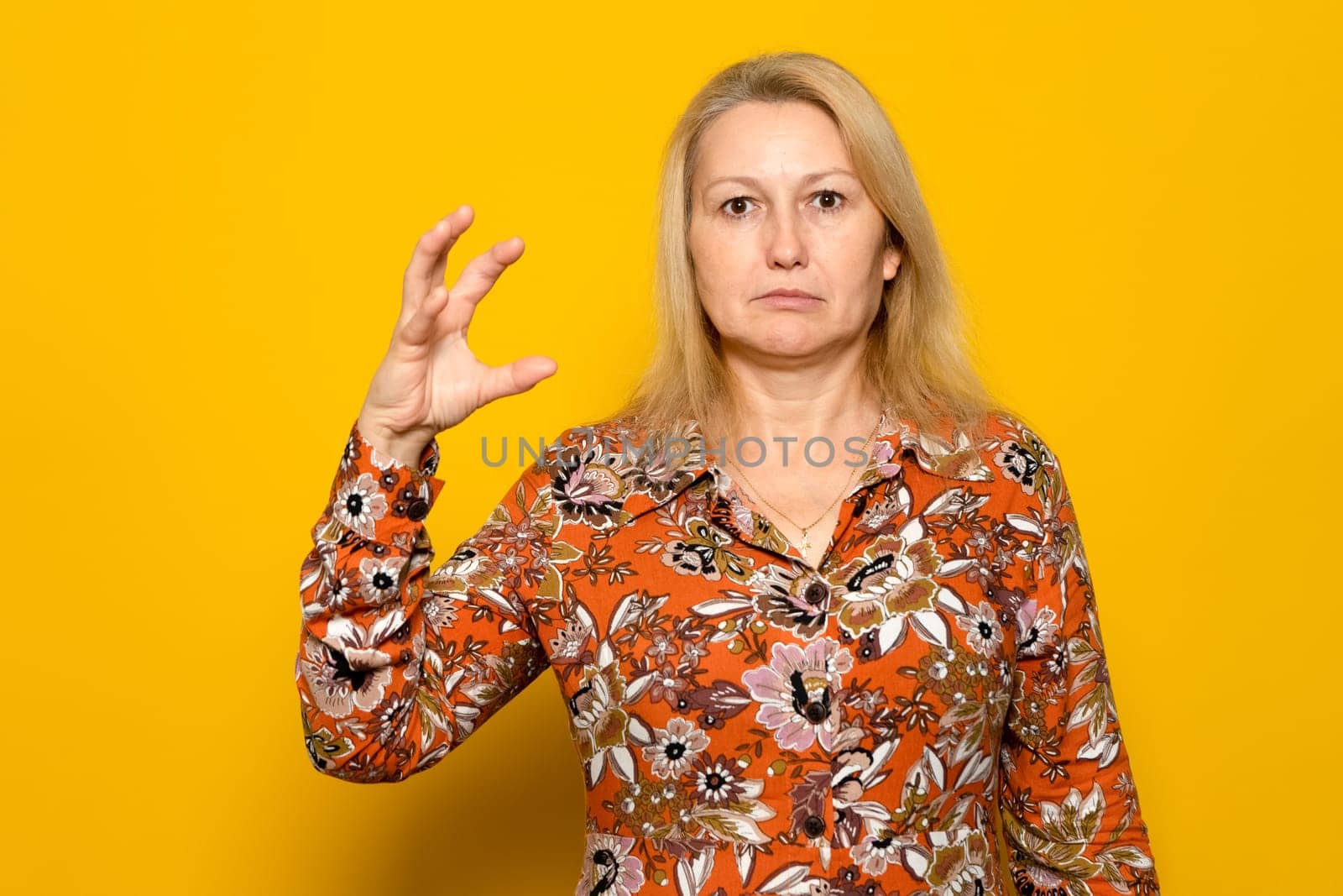 Caucasian blonde female with raised hand in the form of a claw ready to attack her prey, she is angry and dangerous. Isolated on yellow background