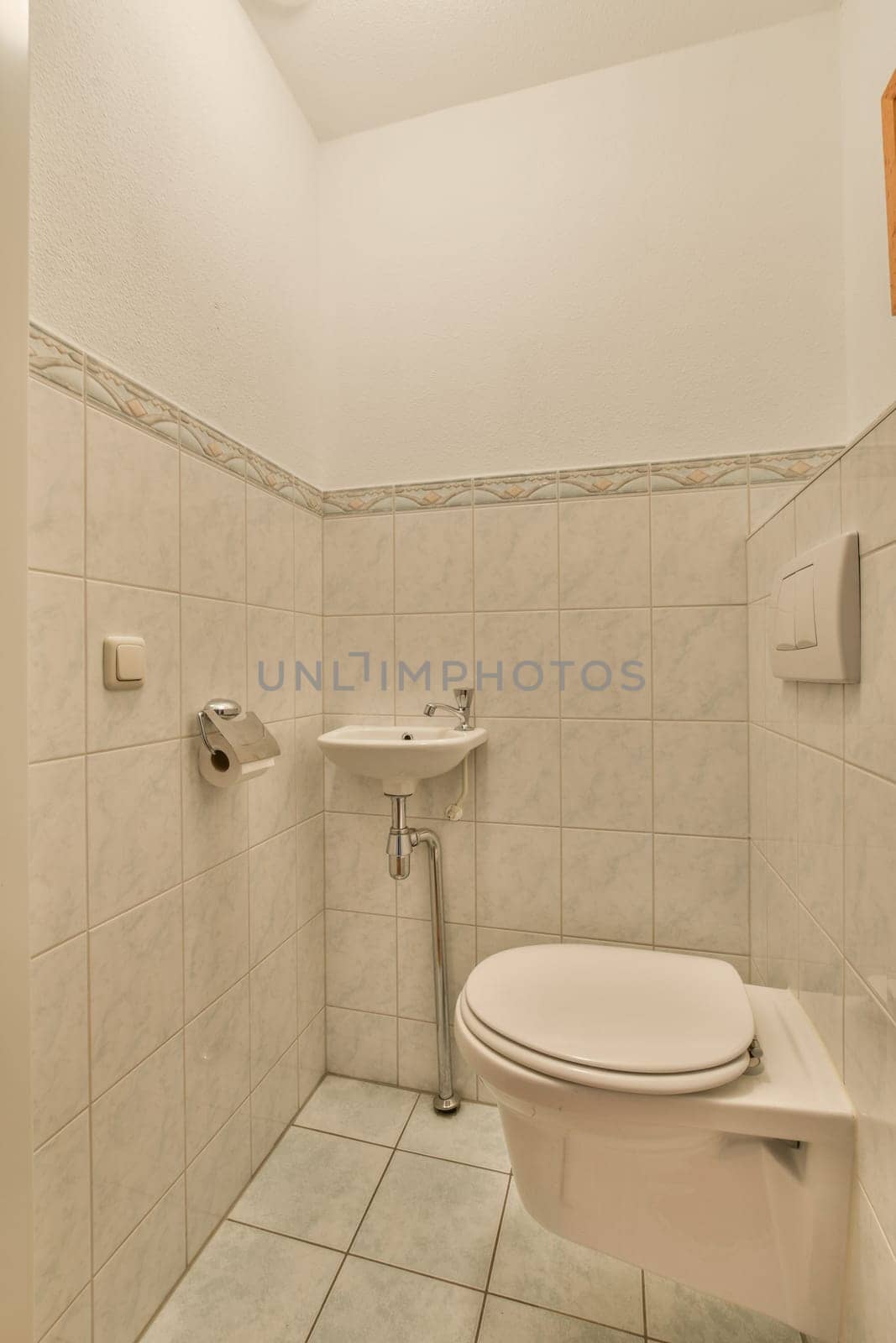 a small bathroom with white tiles on the walls, and a toilet in the corner next to the sink area