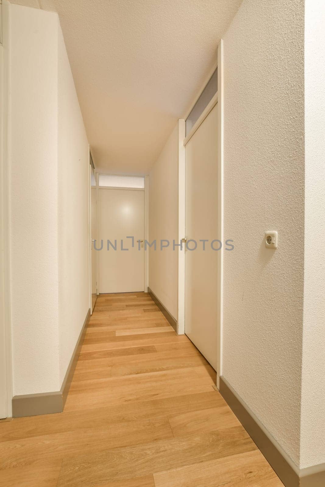 a long hallway with white walls and wood flooring on either side of the room, there is an open door leading to another