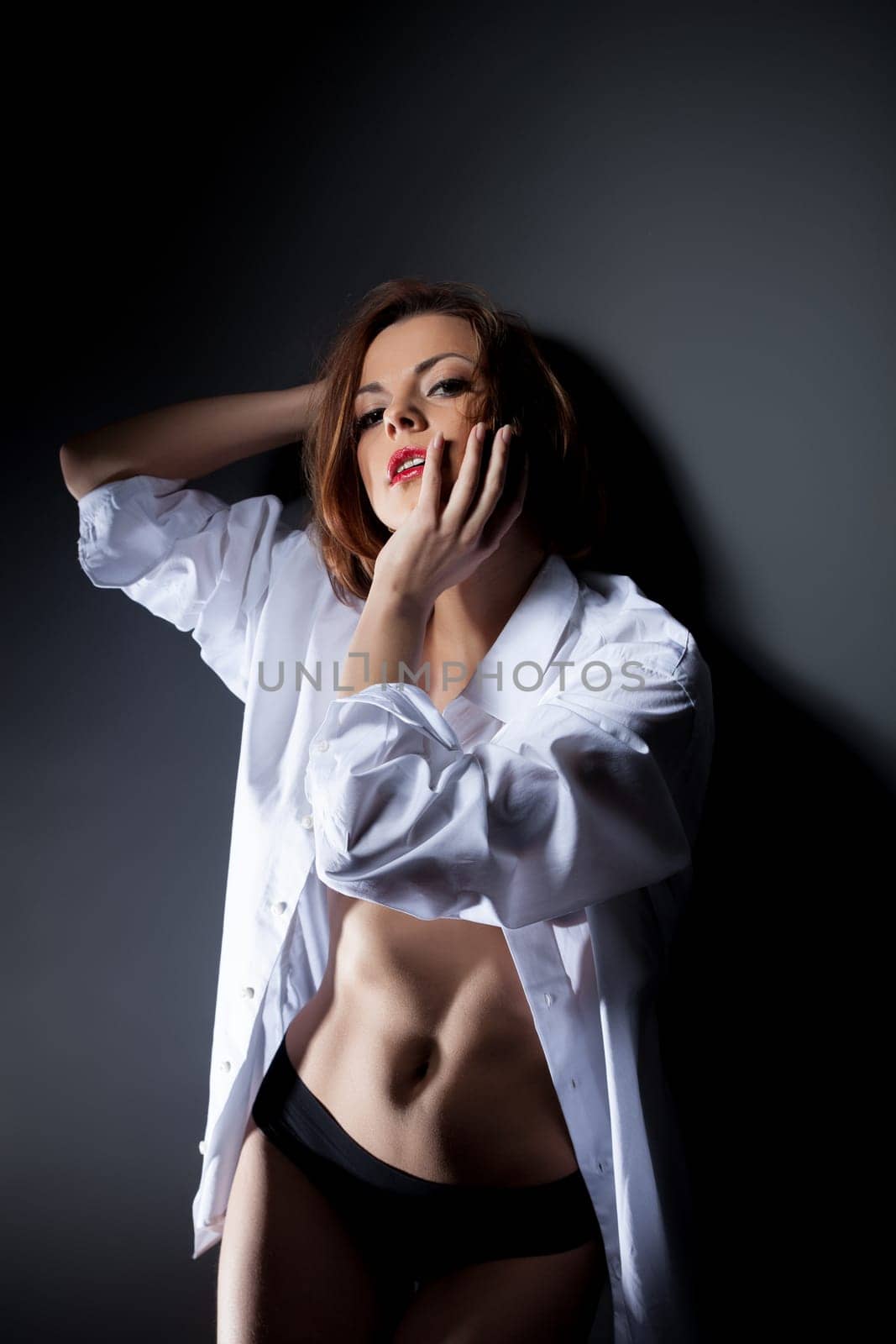 Sexy red-haired woman posing in white blouse, on gray background
