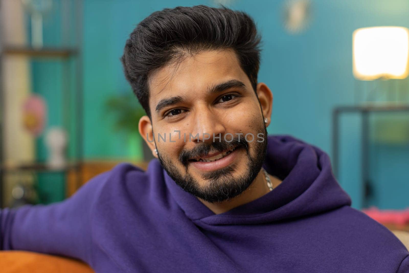 Portrait of happy calm indian man at home couch smiling friendly, glad expression looking away dreaming resting, relaxation feel satisfied concept good news, celebrate win. Hindu guy in living room