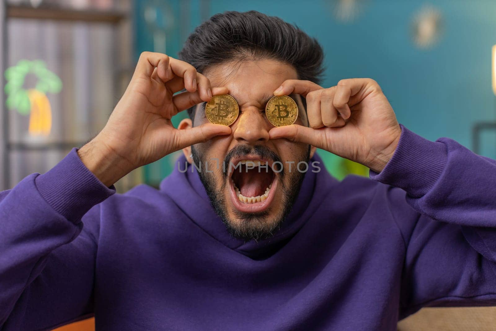 Indian man freelancer holding two gold coins successful developer programmer. Hindu guy stock trader earning bitcoins after online monitoring trading operations. Increasing wealth financial prosperity