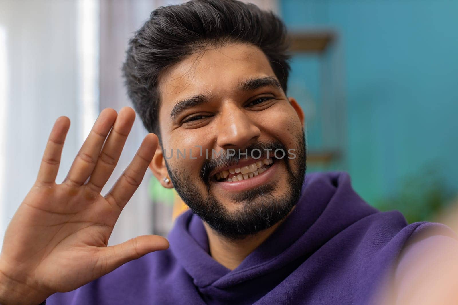 POV of indian man blogger taking selfie on smartphone, communicating video call online with social media subscribers followers, recording vlog stories. Young hindu guy at home apartment room on couch