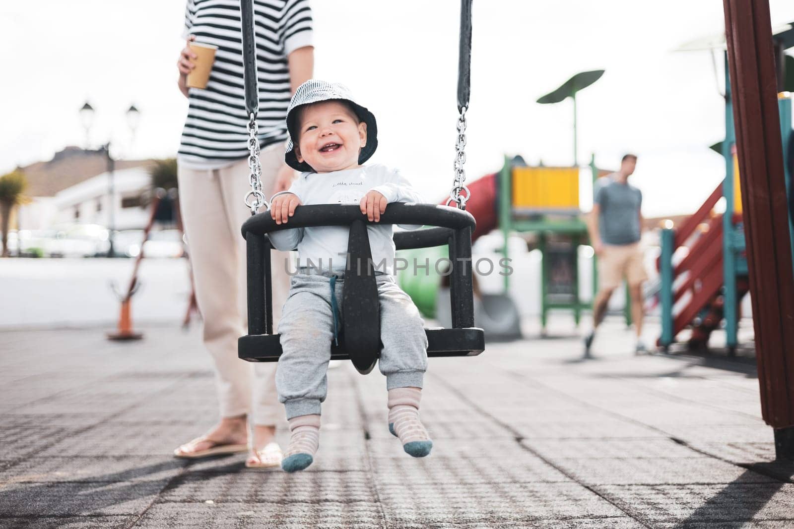 Mother pushing her infant baby boy child on a swing on playground outdoors. by kasto