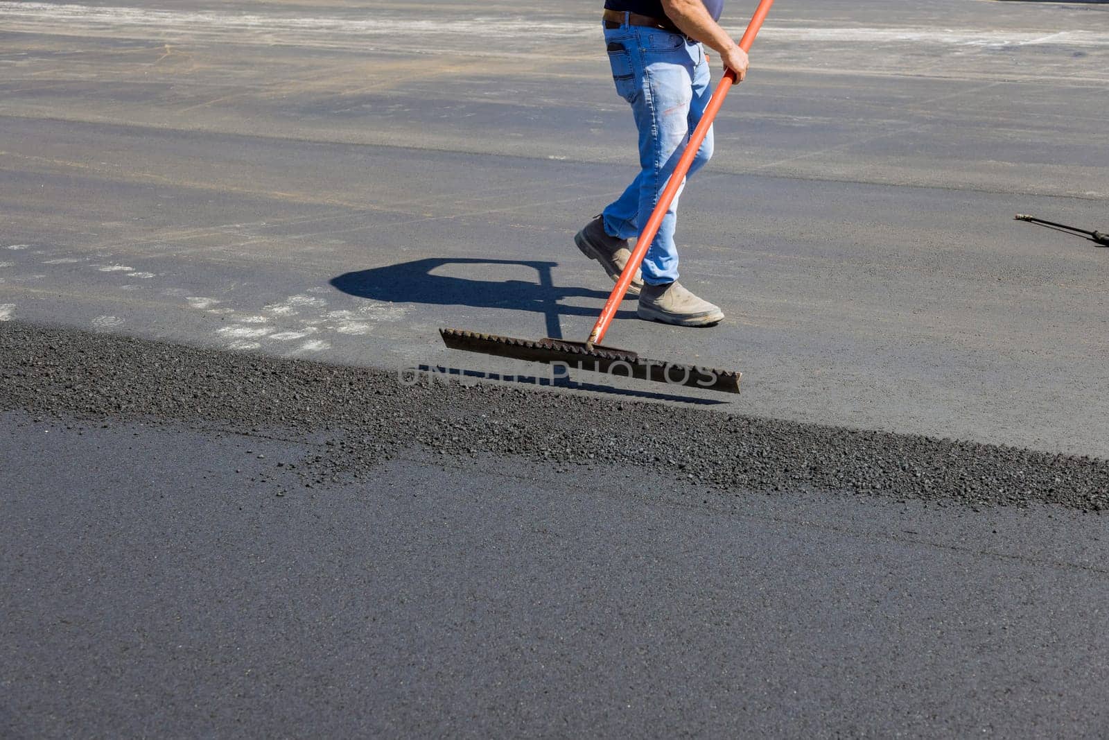 Laying asphalt with working men shoveling black gravel for on the road by ungvar