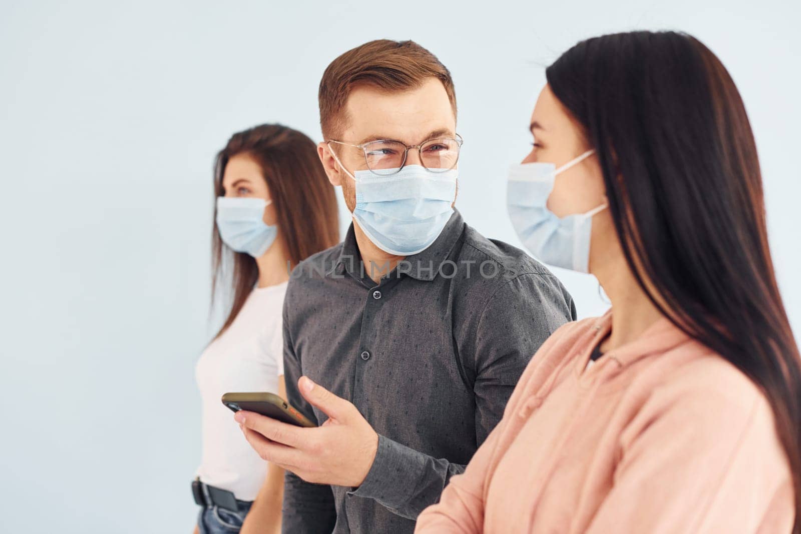 Two women and man standing together indoors in the studio against white wall.