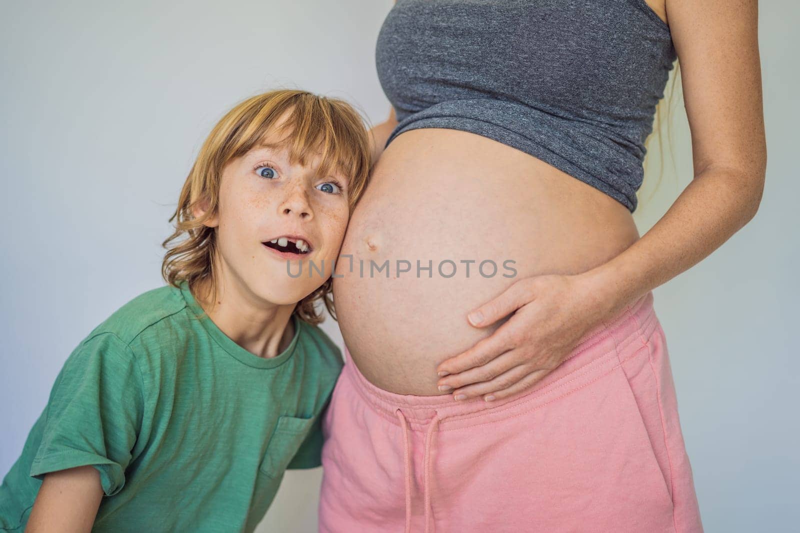 Young beautiful pregnant woman and eldest son. The cute boy leaned his ear against his mother's belly. Expecting a baby in the family concept. Preparing an older child for a younger one.