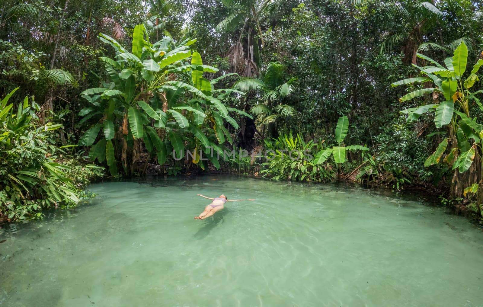 Unrecognizable woman floating on her back in a peaceful and isolated fervedouro in Jalapao, surrounded by lush green rainforest. Perfect for travel ads and vacation brochures.