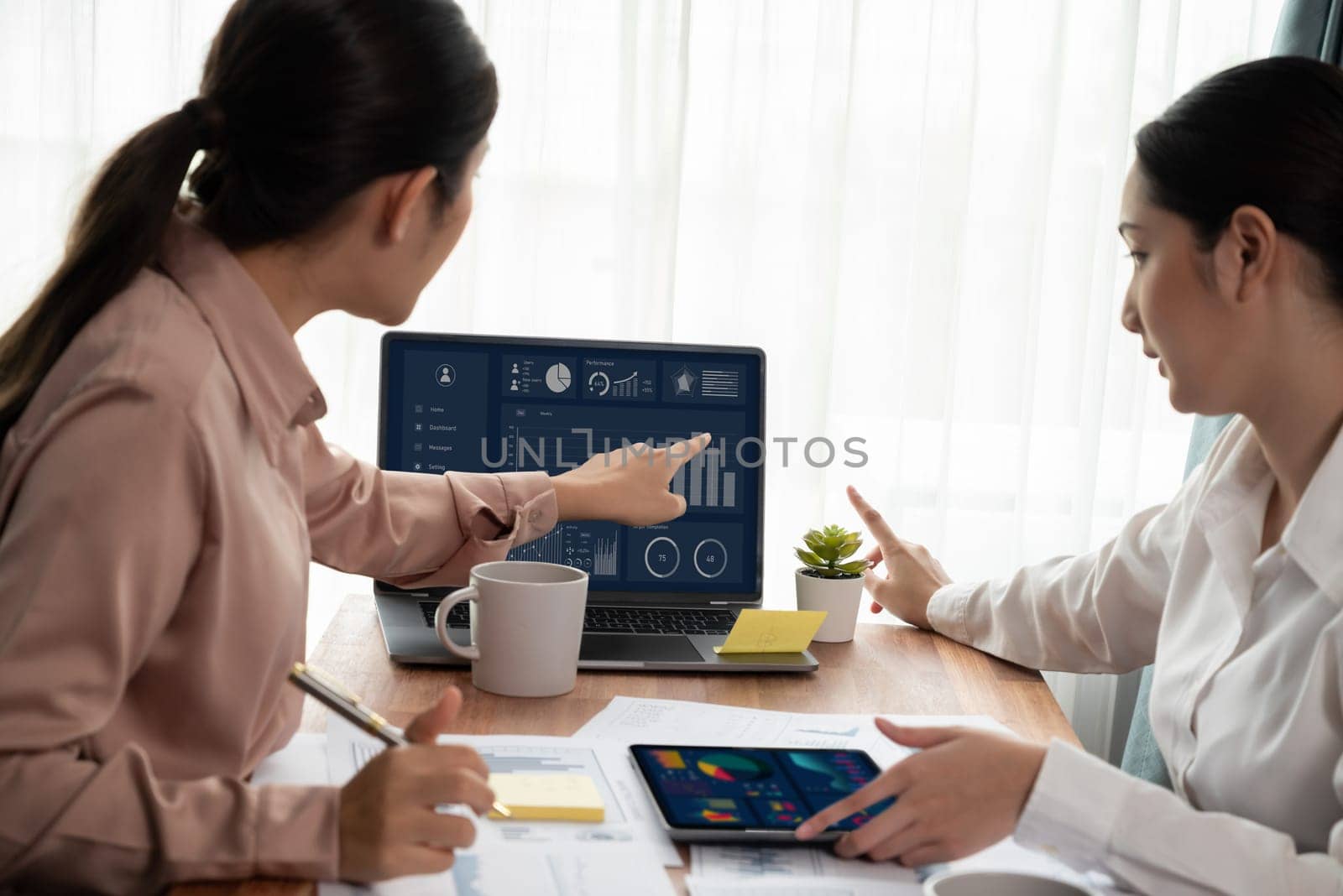 Analyst team colleague discuss financial data on digital dashboard, analyzing charts graph display on laptop and tablet screen. Modern office use business intelligence to plan marketing. Enthusiastic