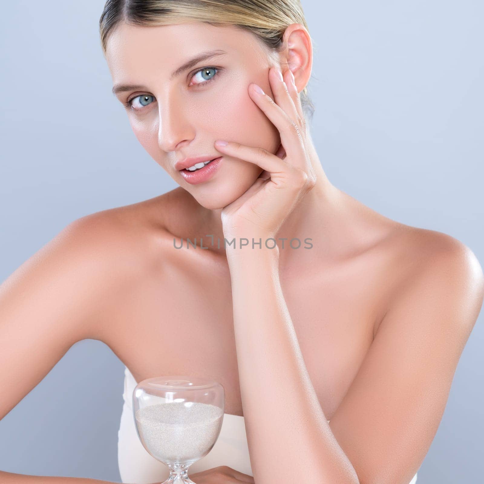 Alluring beauty model using hourglass in beauty concept of anti-aging skincare treatment for woman. Beautiful caucasian women portrait with perfect smooth clean skin in isolated background.