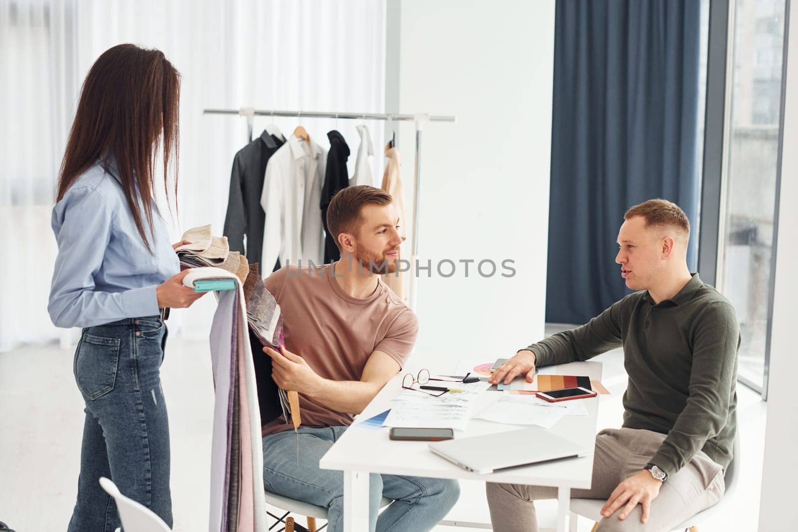 Cloth and fashion business. Three people works in the office by sitting by the table.