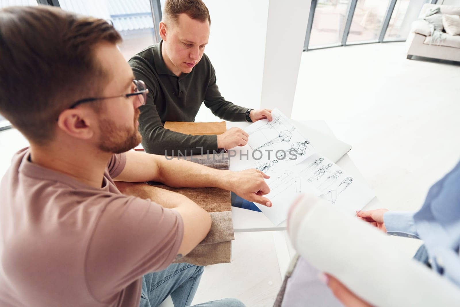 Cloth and fashion business. Three people works in the office by sitting by the table by Standret