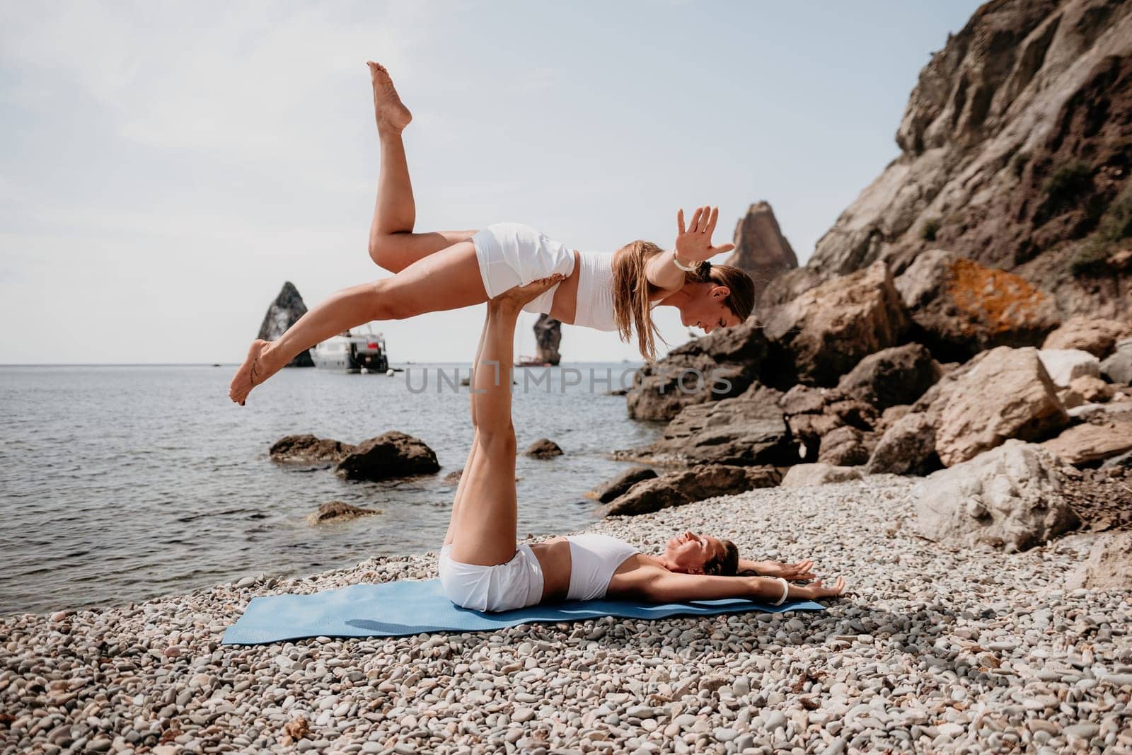 Woman sea yoga. Two Happy women meditating in yoga pose on the beach, ocean and rock mountains. Motivation and inspirational fit and exercising. Healthy lifestyle outdoors in nature, fitness concept. by panophotograph