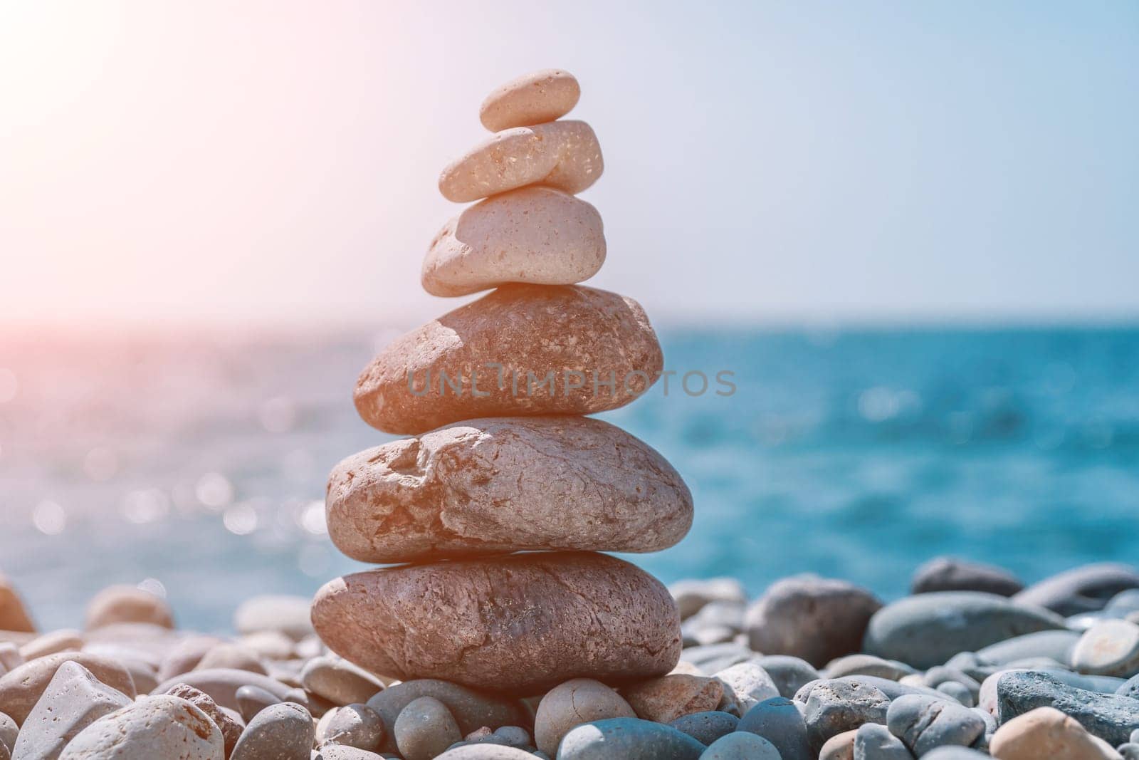 Balanced Pebbles Pyramid on the Beach on Sunny Day and Clear Sky at Sunset. Blue Sea on Background Selective focus, zen stones on sea beach, meditation, spa, harmony, calm, balance concept.