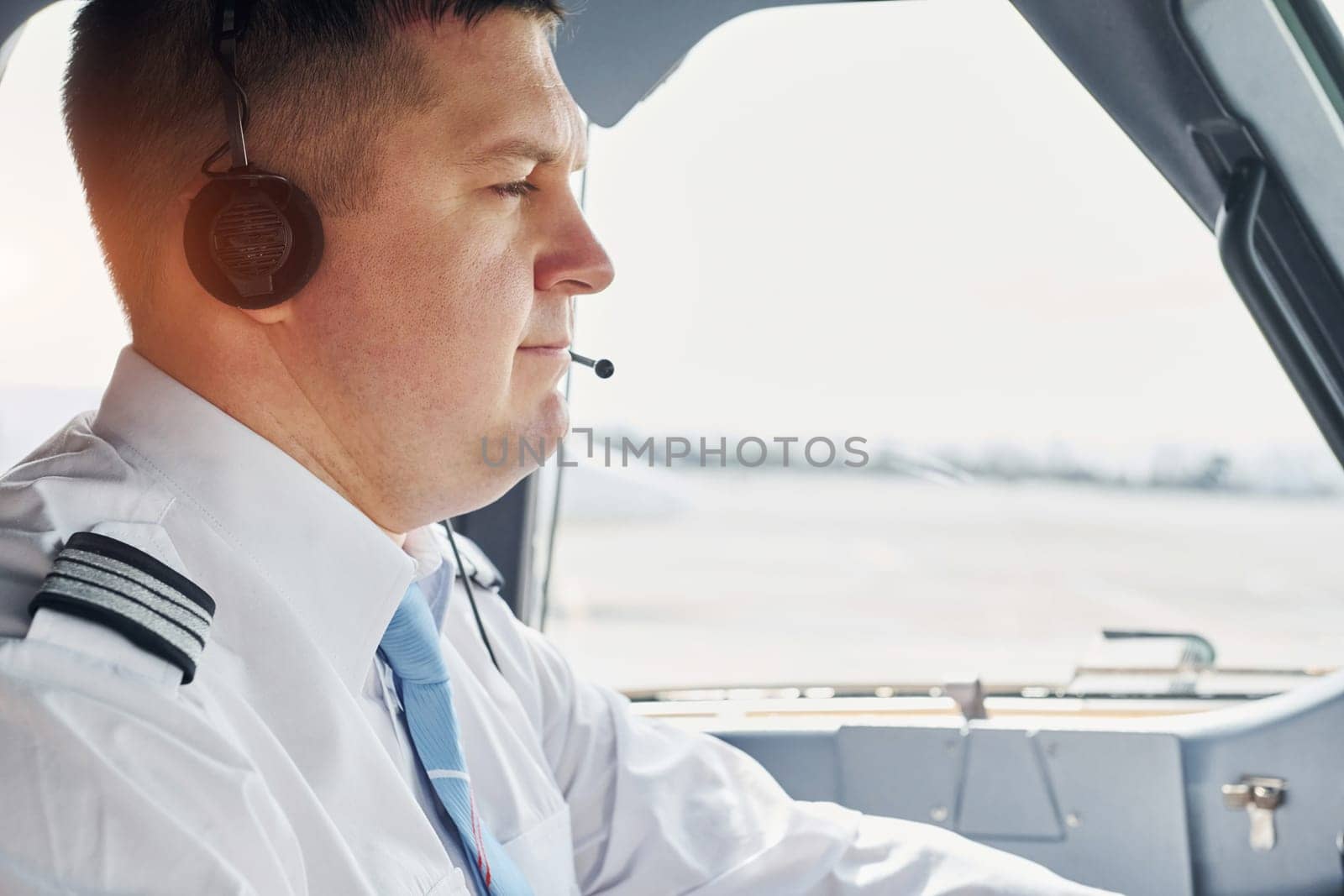 Side view. Pilot in formal wear sits in the cockpit and controls airplane by Standret