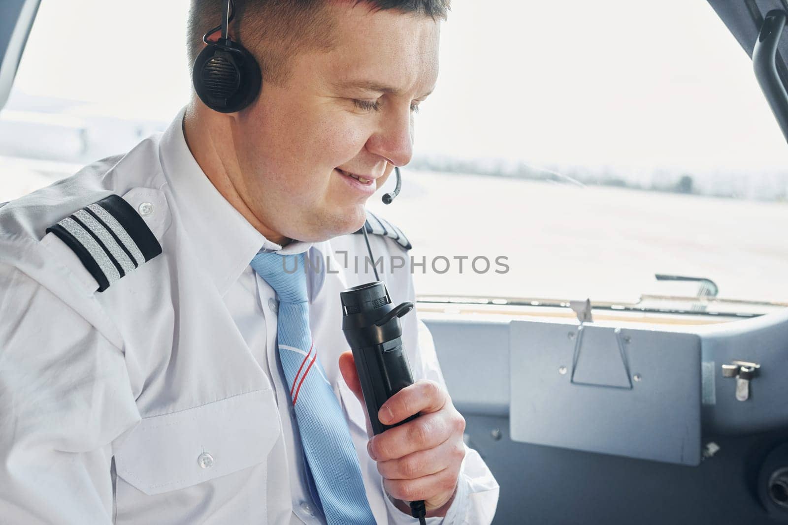 Talks to a mic. Pilot in formal wear sits in the cockpit and controls airplane.