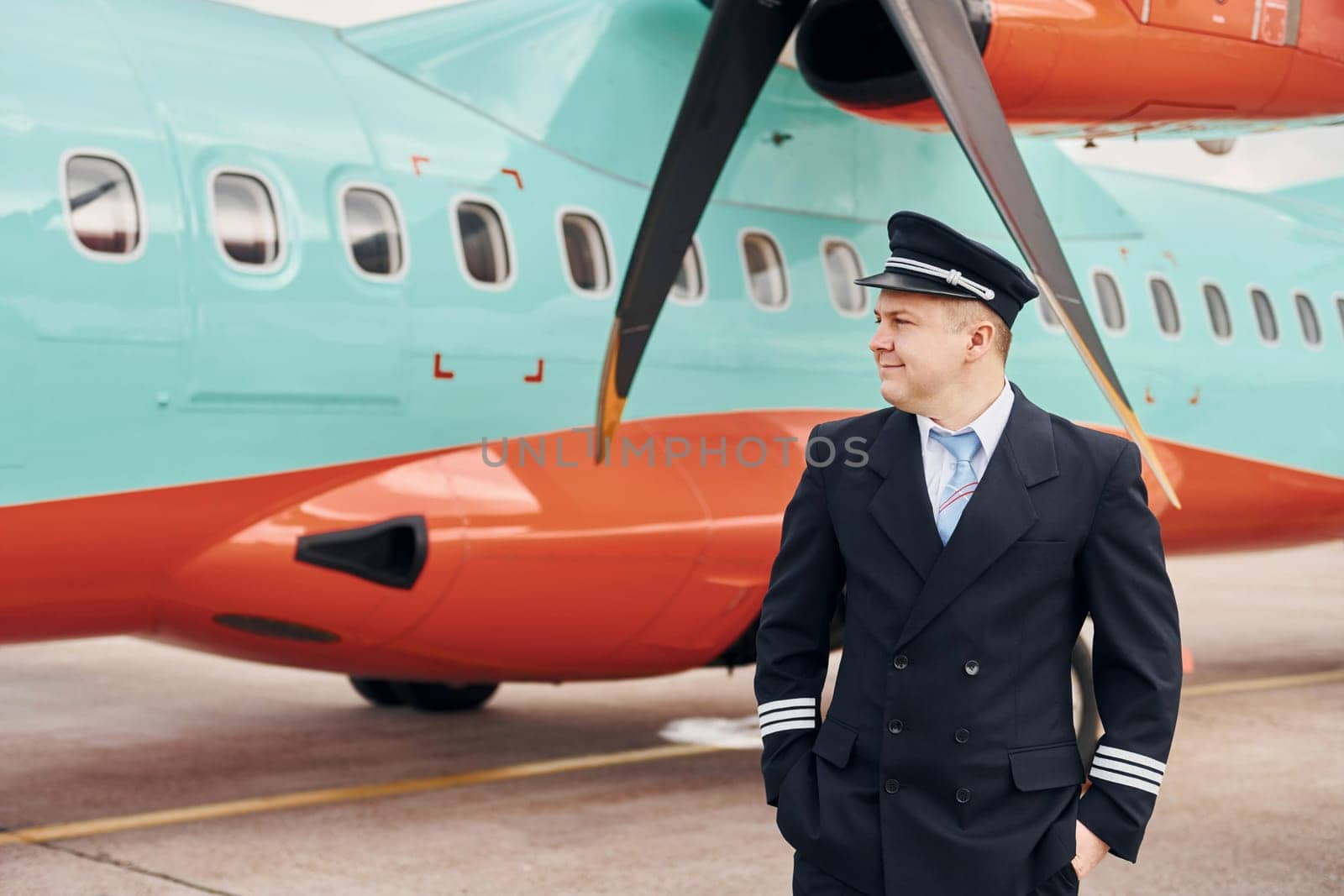 Experienced pilot in uniform standing outside near plane by Standret