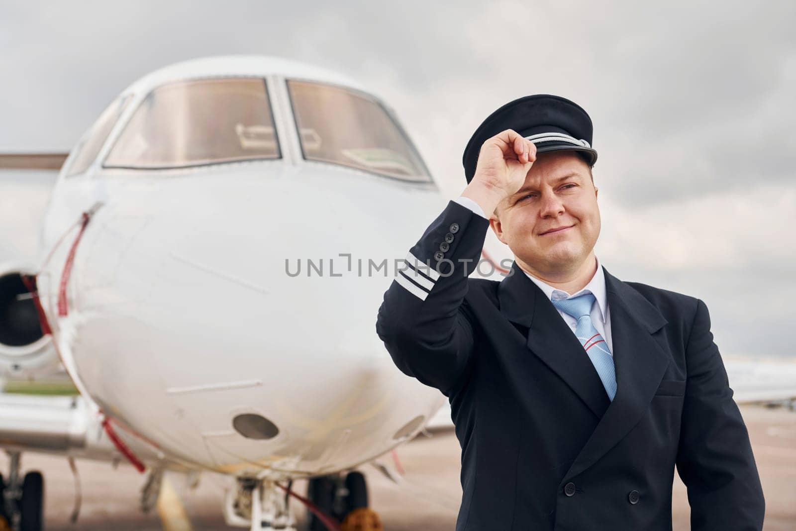 Experienced pilot in uniform standing outside near plane by Standret