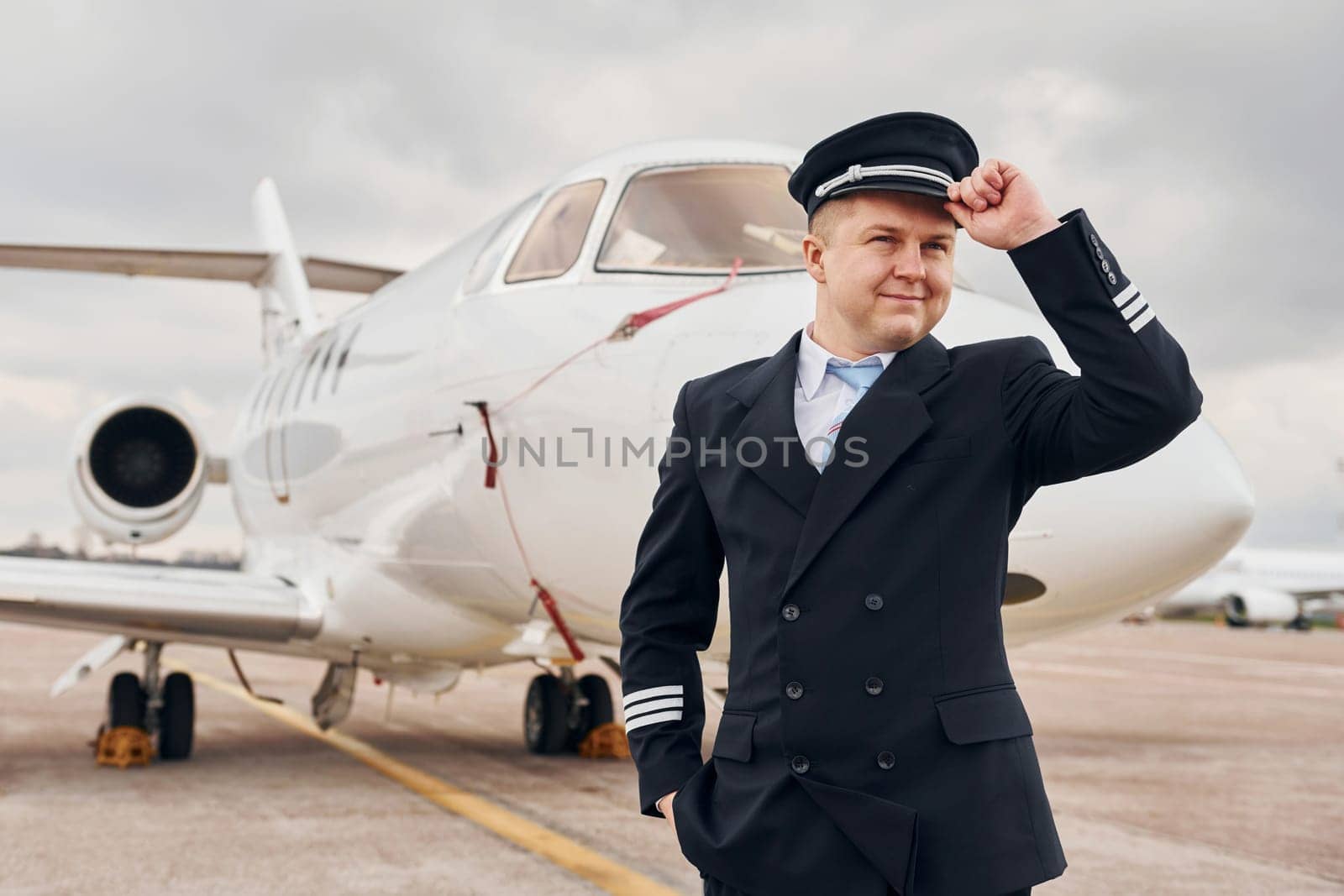 Posing for a camera. Experienced pilot in uniform standing outside near plane.