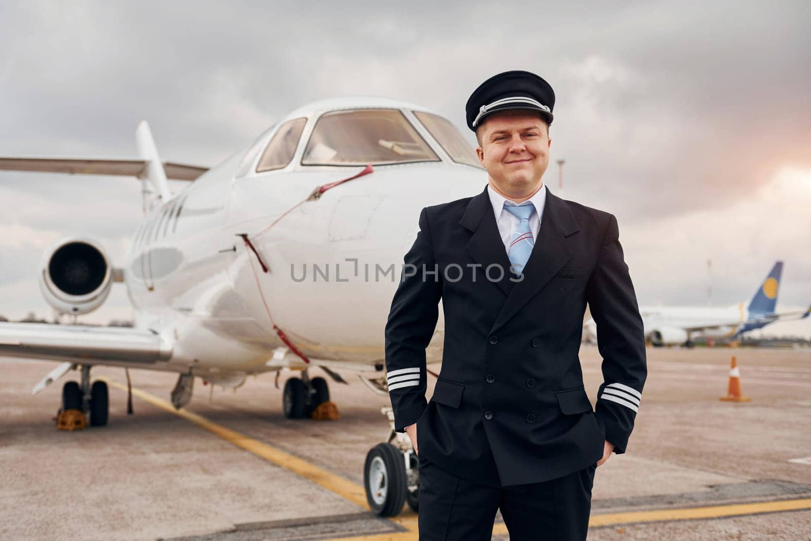 Posing for a camera. Experienced pilot in uniform standing outside near plane.