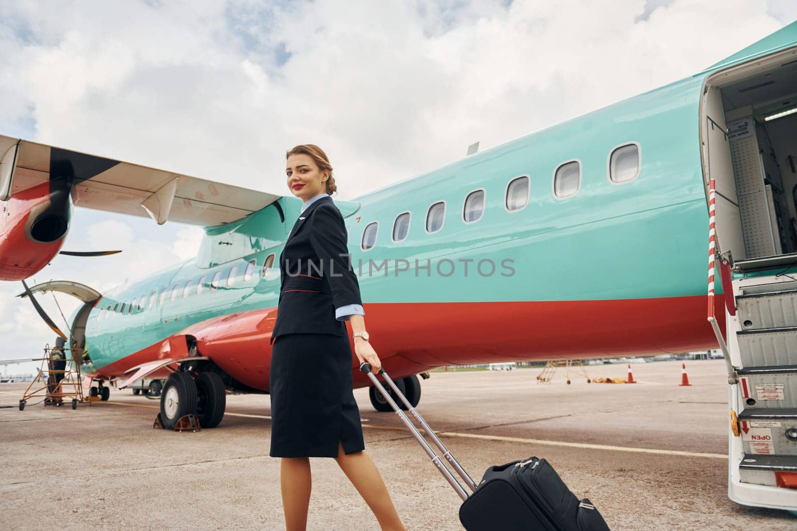 Young woman with luggage is outdoors near airplane.