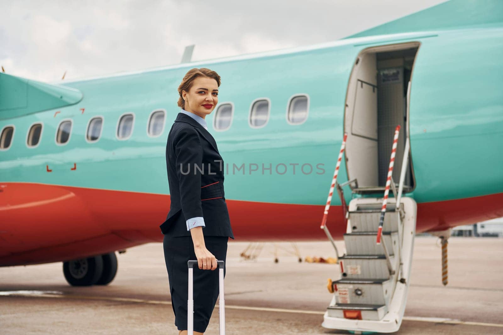 Young woman with luggage is outdoors near airplane.
