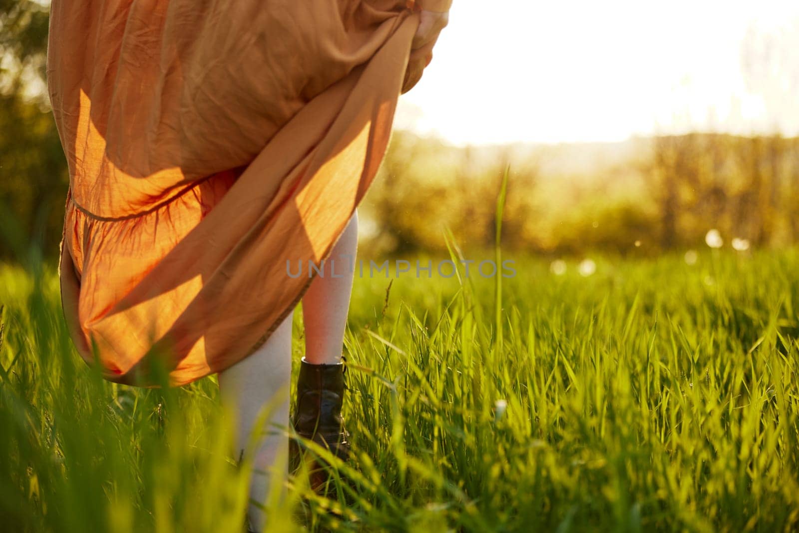 close horizontal photo of women's legs in a long orange skirt, with sunset lighting by Vichizh