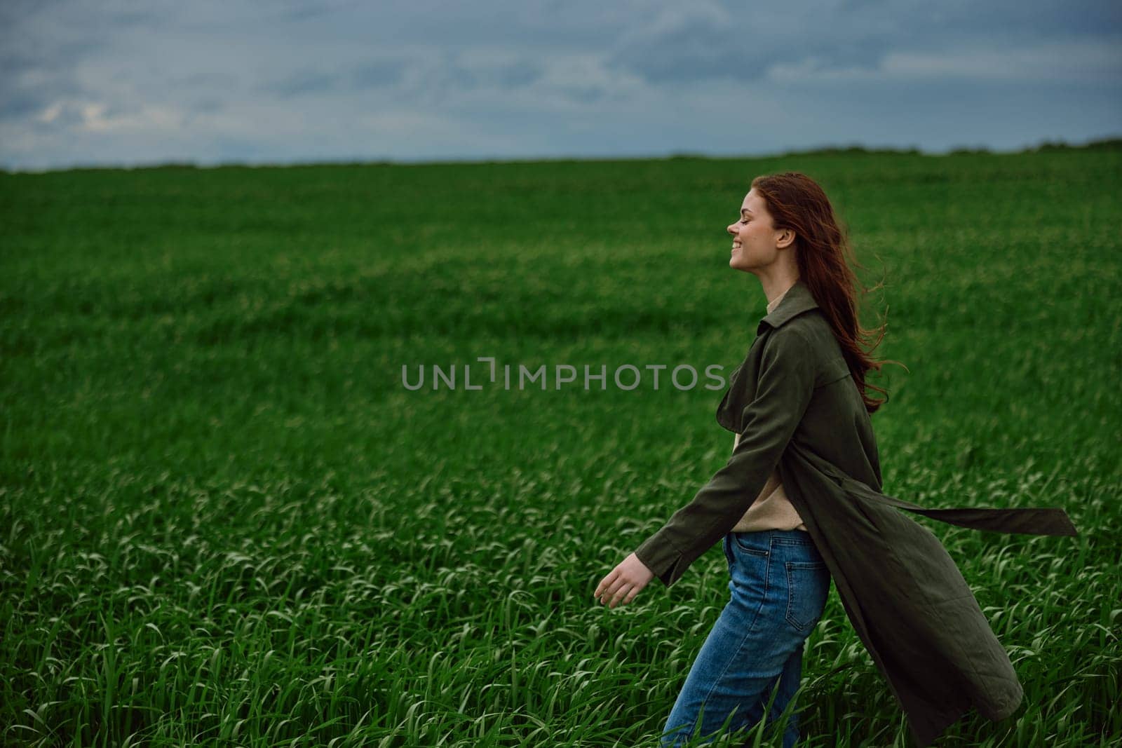 red-haired, happy woman stands in a green field in rainy weather. Emotions, harmony with nature by Vichizh
