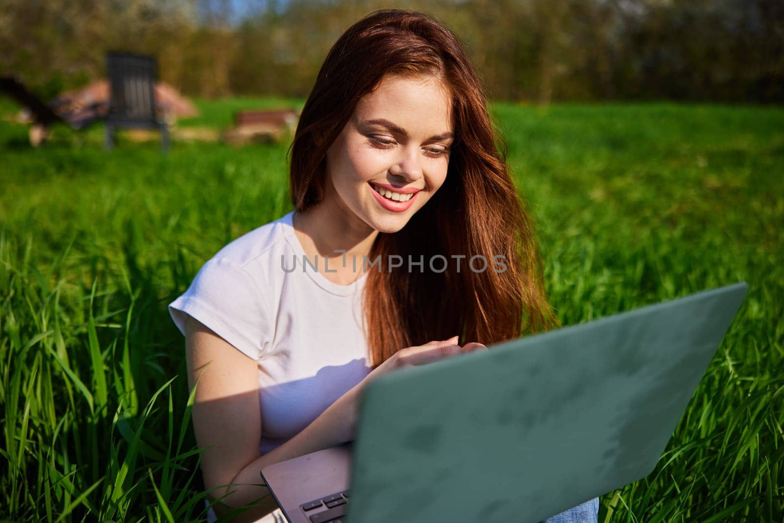 happy, joyful woman working on a laptop while sitting in a field by Vichizh