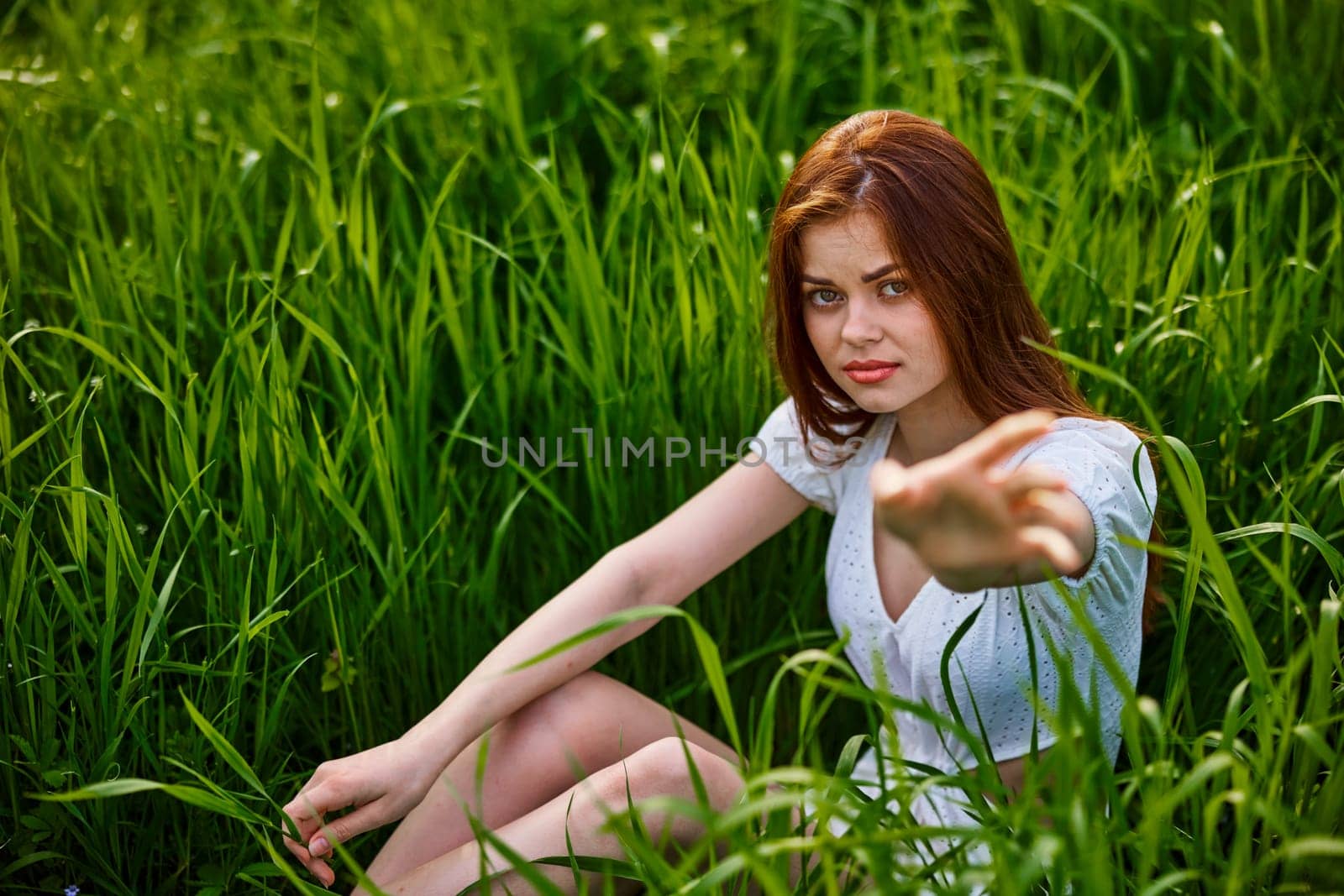 the girl sits in the tall grass and extends her hand for help by Vichizh