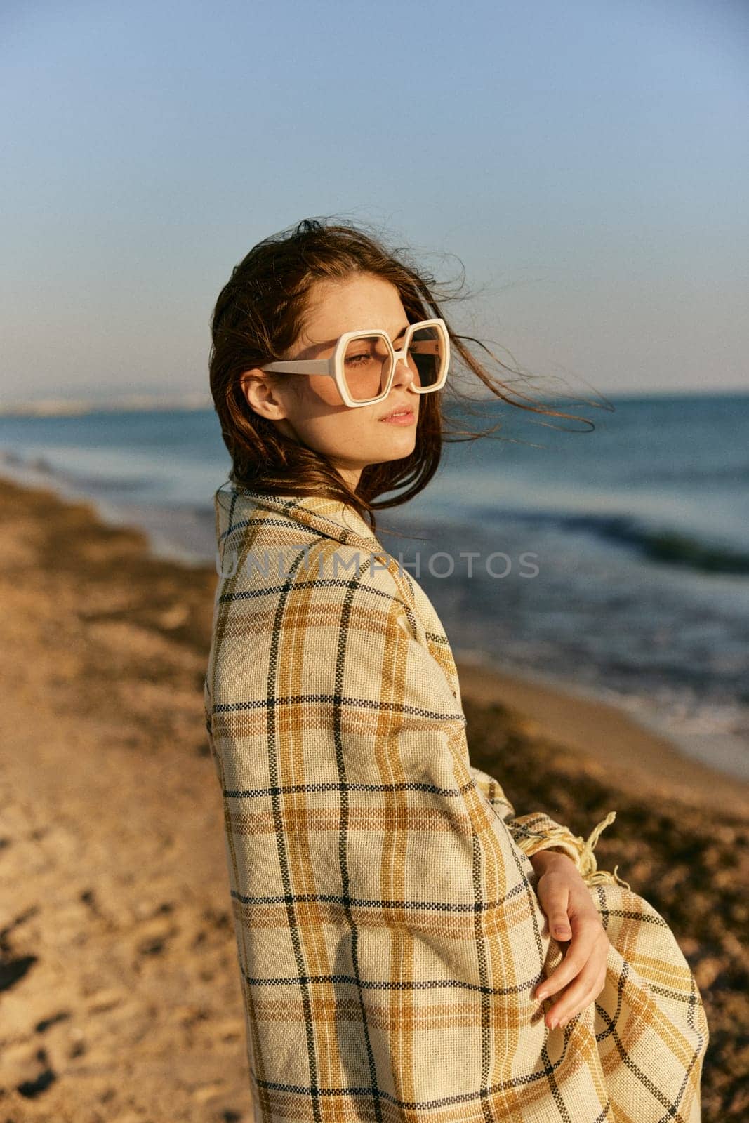 portrait of a beautiful woman with red hair blown by the wind on the sea coast wrapped in a plaid. High quality photo