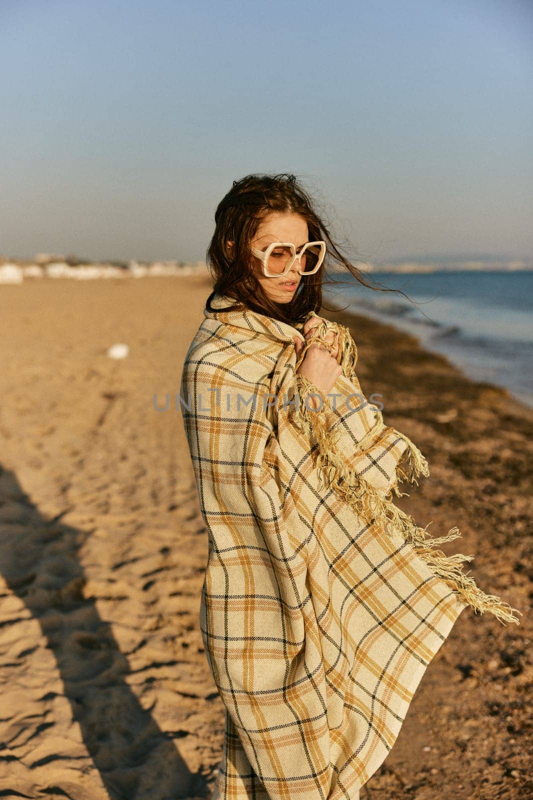 a beautiful woman wrapped in a plaid stands on the seashore against the backdrop of sunset. High quality photo