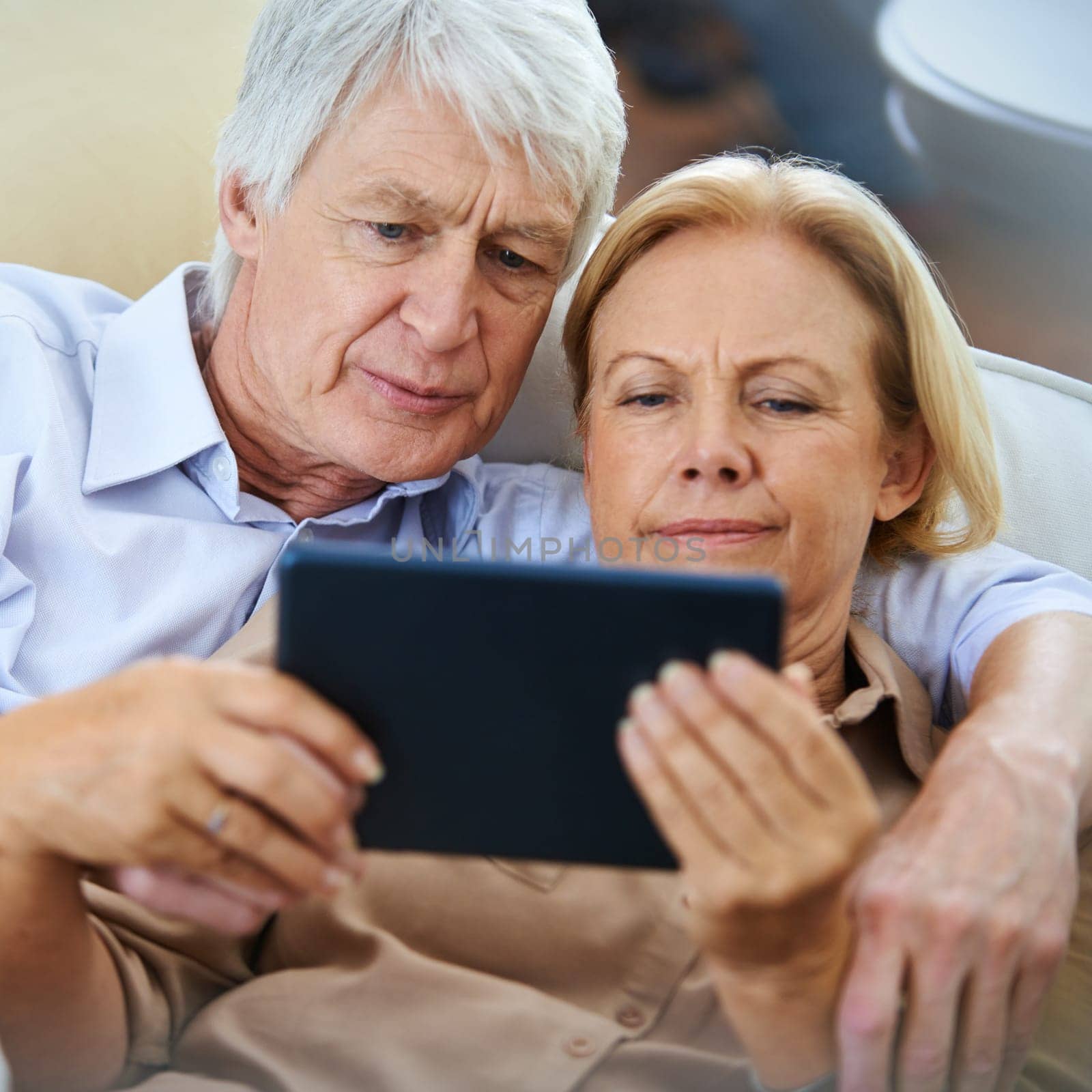 Making the cozy connection. a happy elderly couple watching something on a digital tablet while relaxing on their sofa. by YuriArcurs