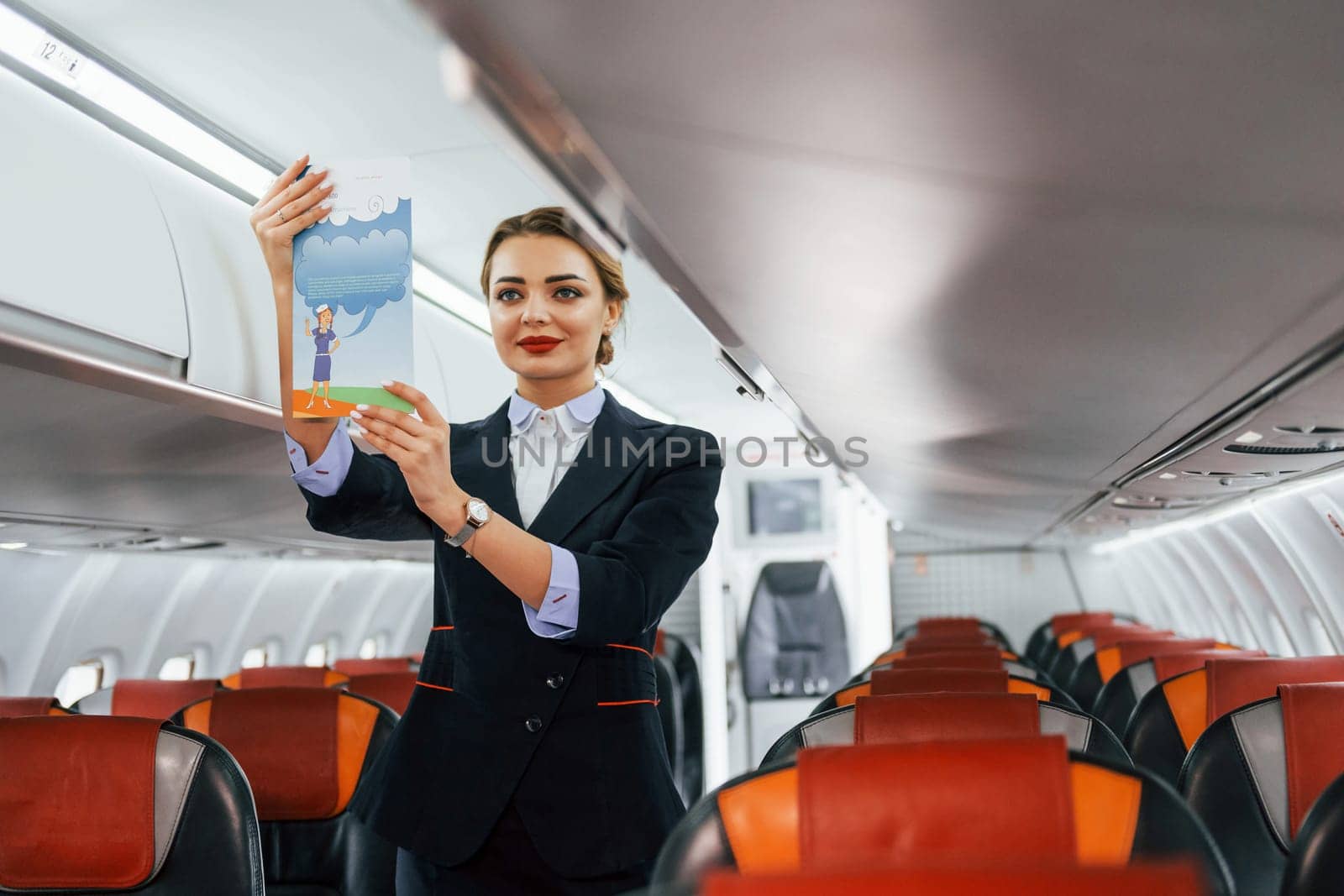 Holds paper with instrucitons. Young stewardess on the work in the passanger airplane.