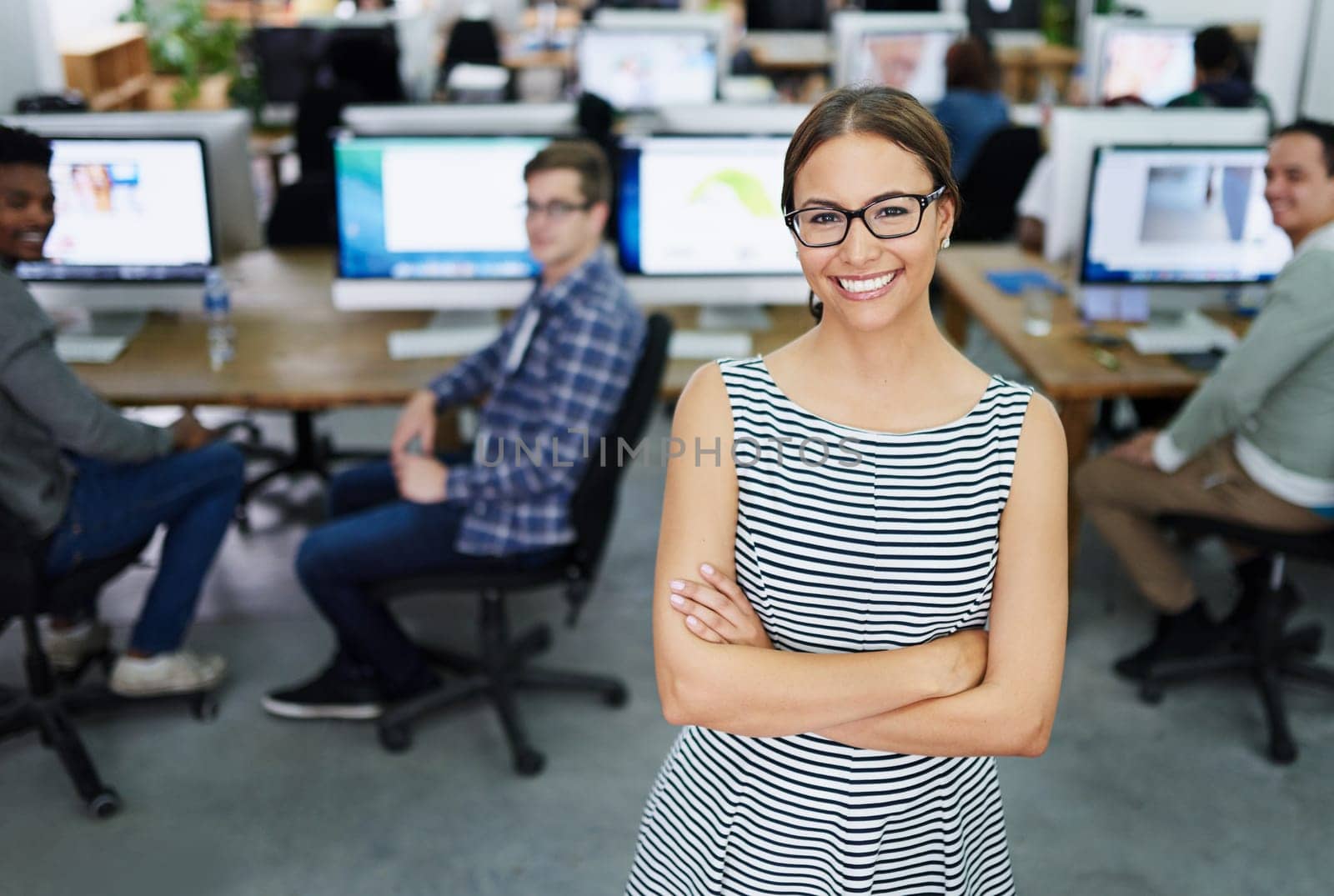 Its a great working environment. Portrait of a smiling young designer standing in an office with colleagues working in the background