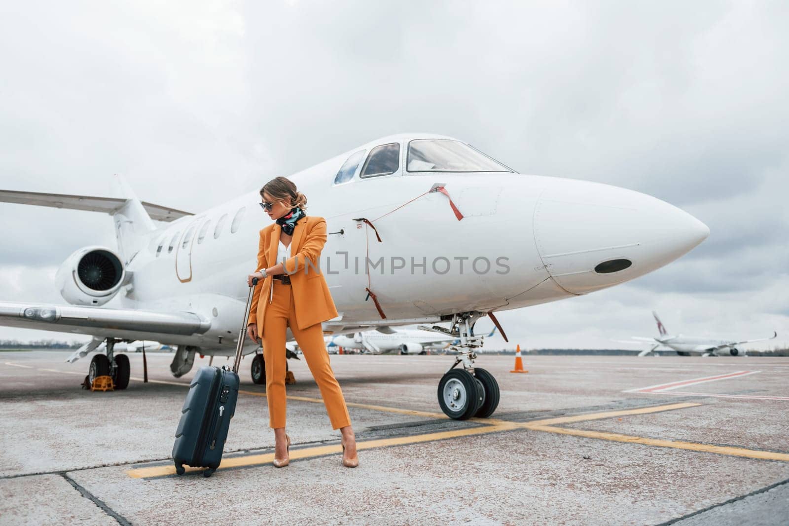 Passenger woman that is in yellow clothes, sunglasses and with luggage is outdoors near plane.