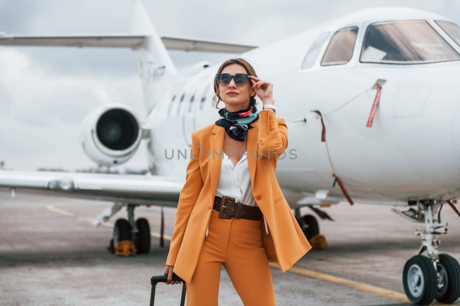 Cloudy weather. Passenger woman that is in yellow clothes, sunglasses and with luggage by Standret