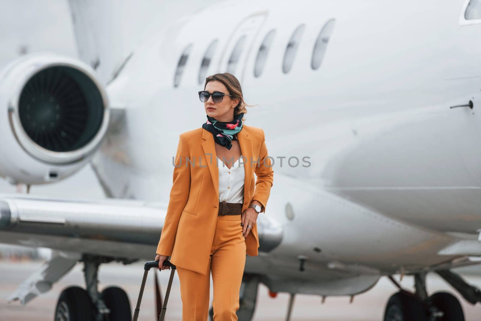 Cloudy weather. Passenger woman that is in yellow clothes, sunglasses and with luggage by Standret