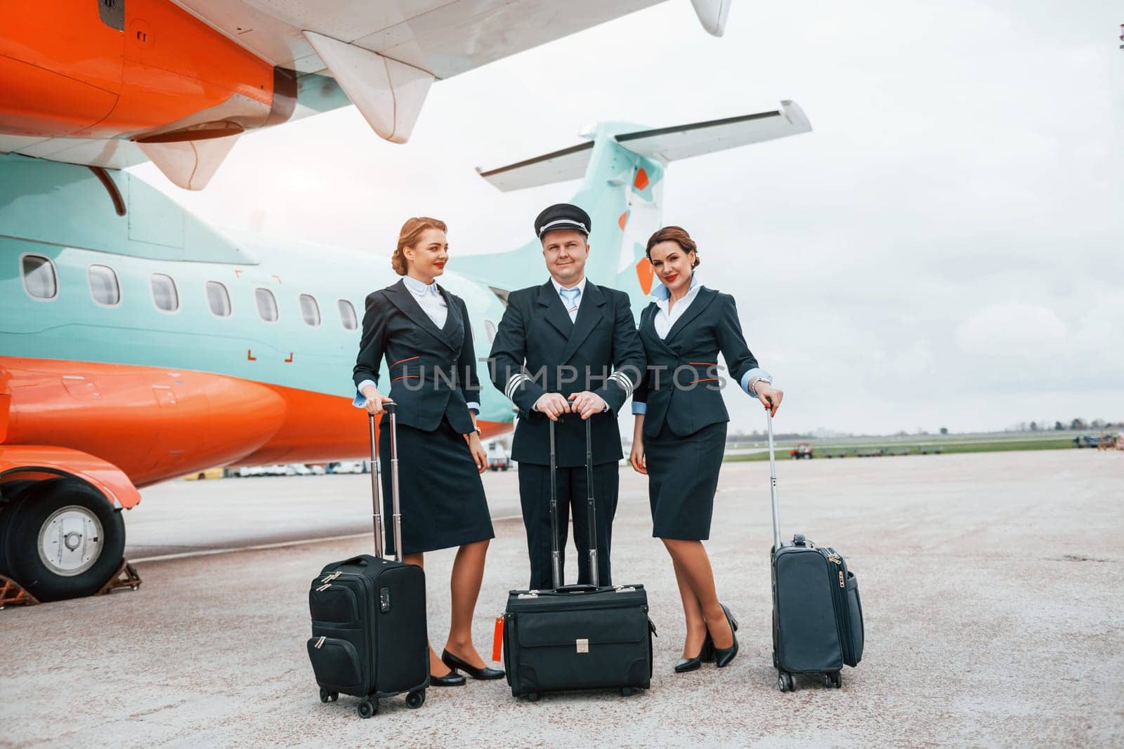 With luggage. Aircraft crew in work uniform is together outdoors near plane.