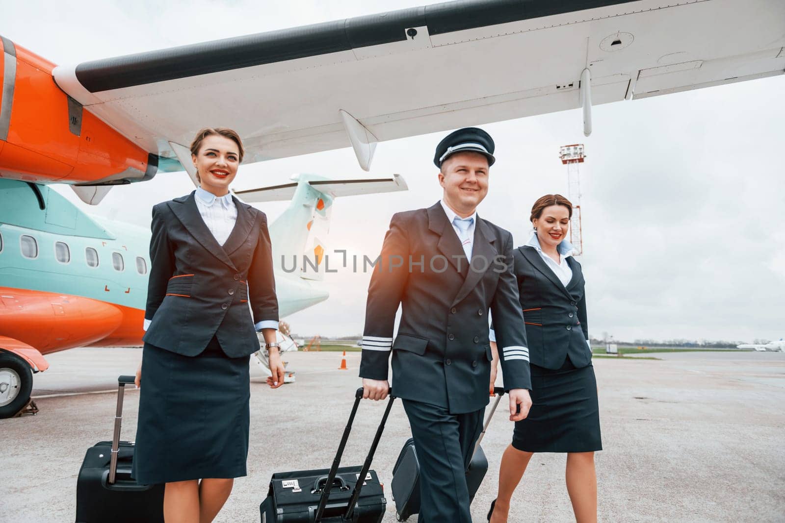 With luggage. Aircraft crew in work uniform is together outdoors near plane by Standret