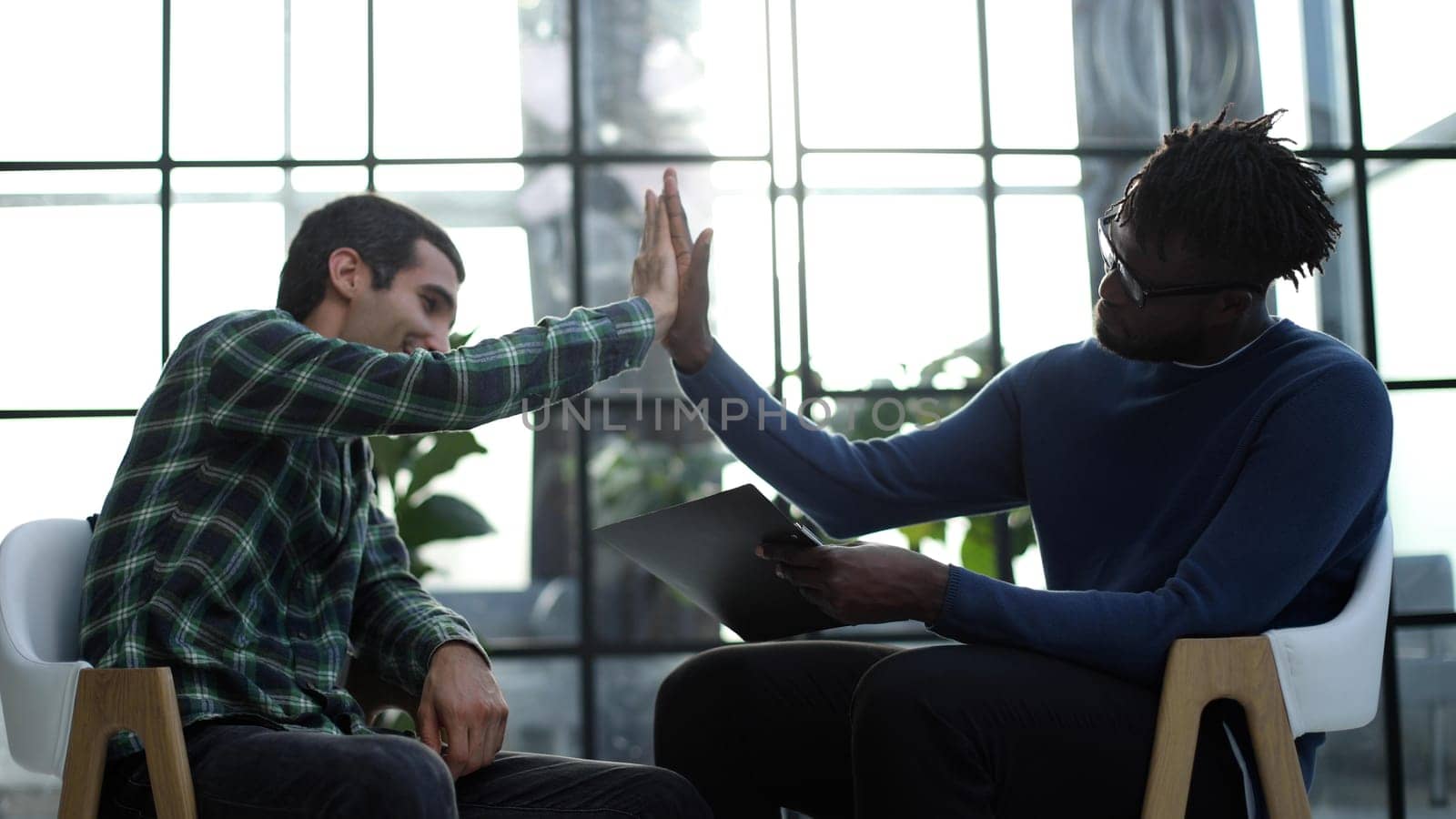 Business partners shaking hands sit on chairs in office lobby start or finish successful negotiations.