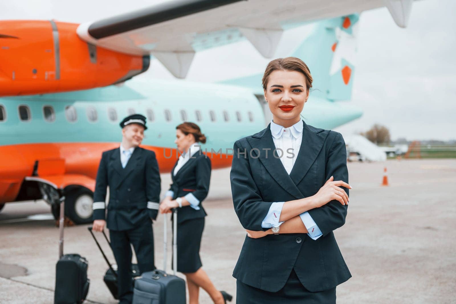 With luggage. Aircraft crew in work uniform is together outdoors near plane.