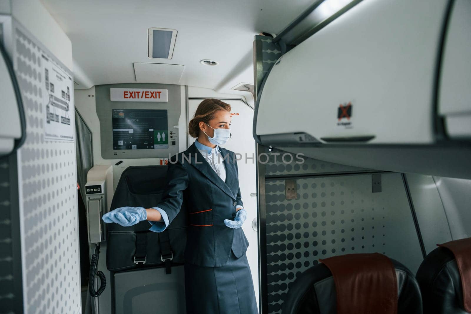 In protective gloves and mask. Young stewardess on the work in the passanger airplane by Standret