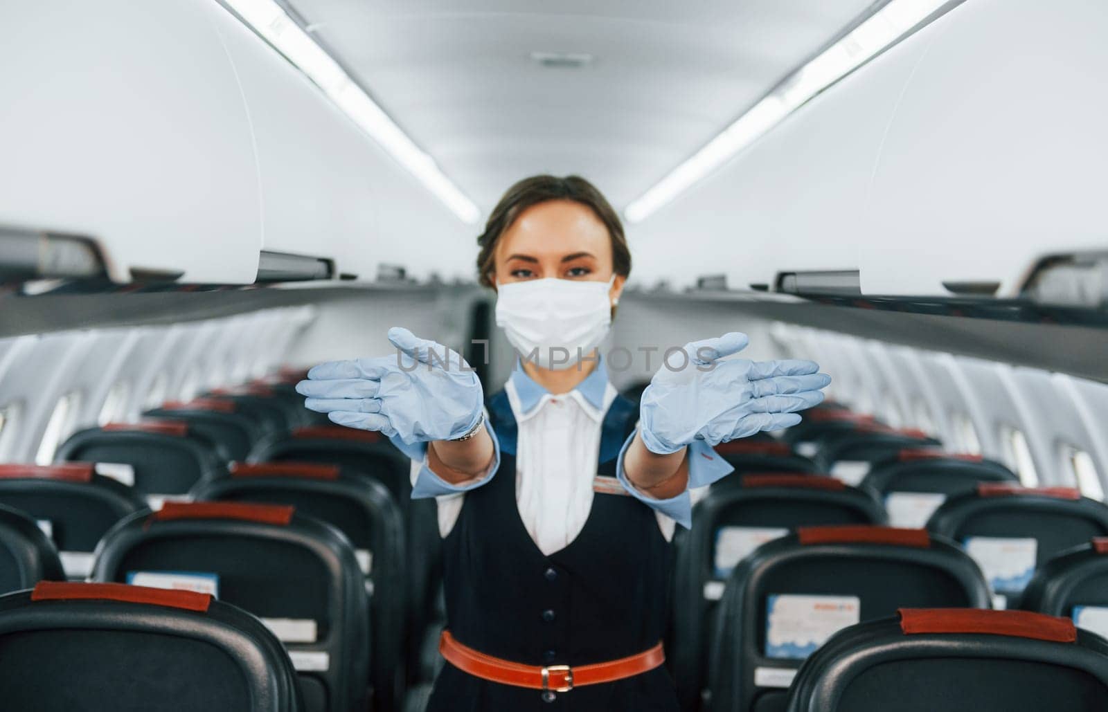 In protective gloves and mask. Young stewardess on the work in the passanger airplane.