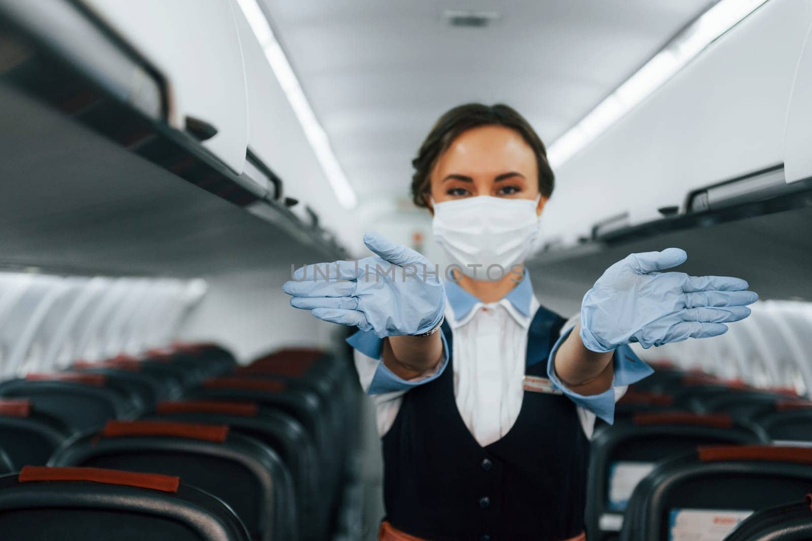 In protective gloves and mask. Young stewardess on the work in the passanger airplane by Standret