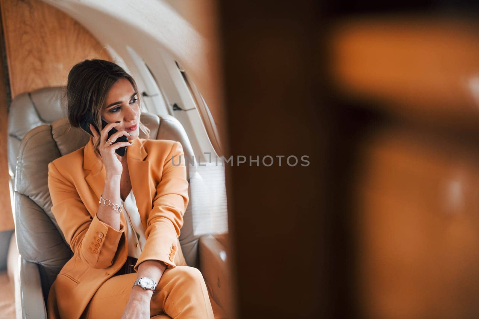 Uses phone. Young passenger woman in yellow clothes is flying in the plane.