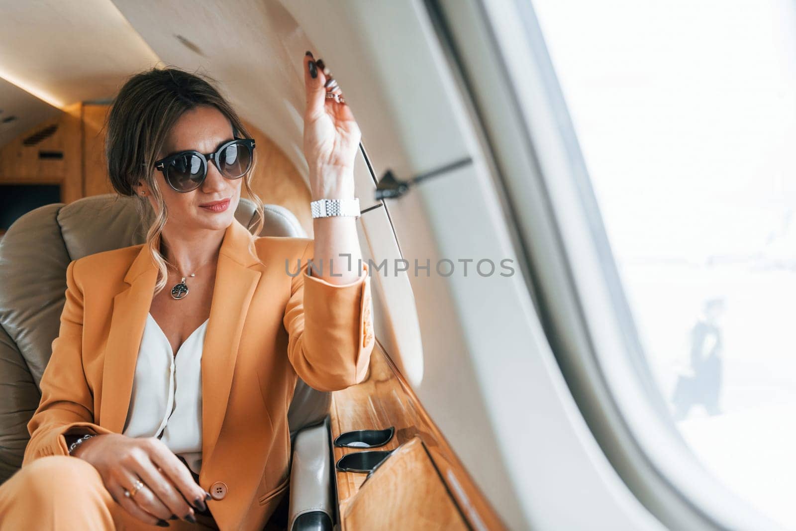 In sunglasses. Young passenger woman in yellow clothes is flying in the plane.