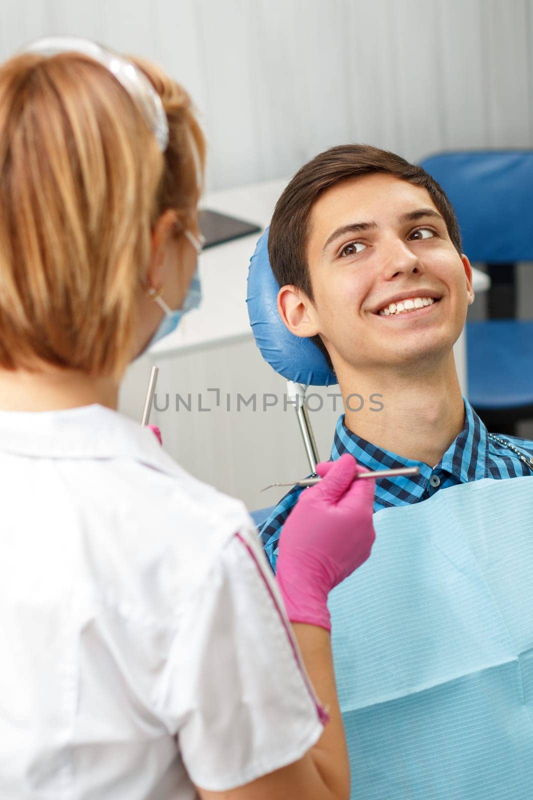 Handsome young man is having dental check up in dental office. Dentist is examining a patient with dental tools