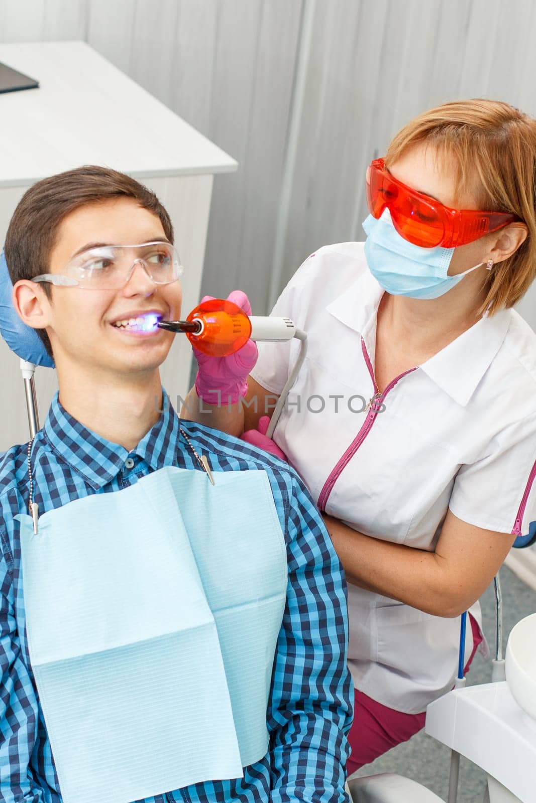Beautiful woman dentist treating teeth in dental office. Doctor wearing glasses, mask, white uniform and pink gloves. Selective focus on a dentist