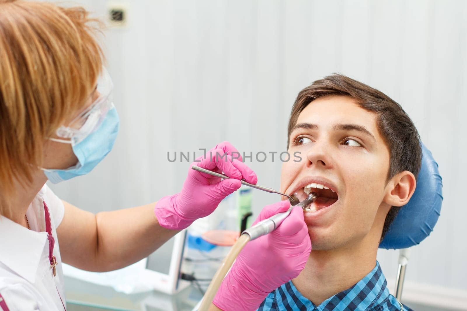 Female dentist is treating a patient tooth in dental office with focus on patient mouth by mvg6894